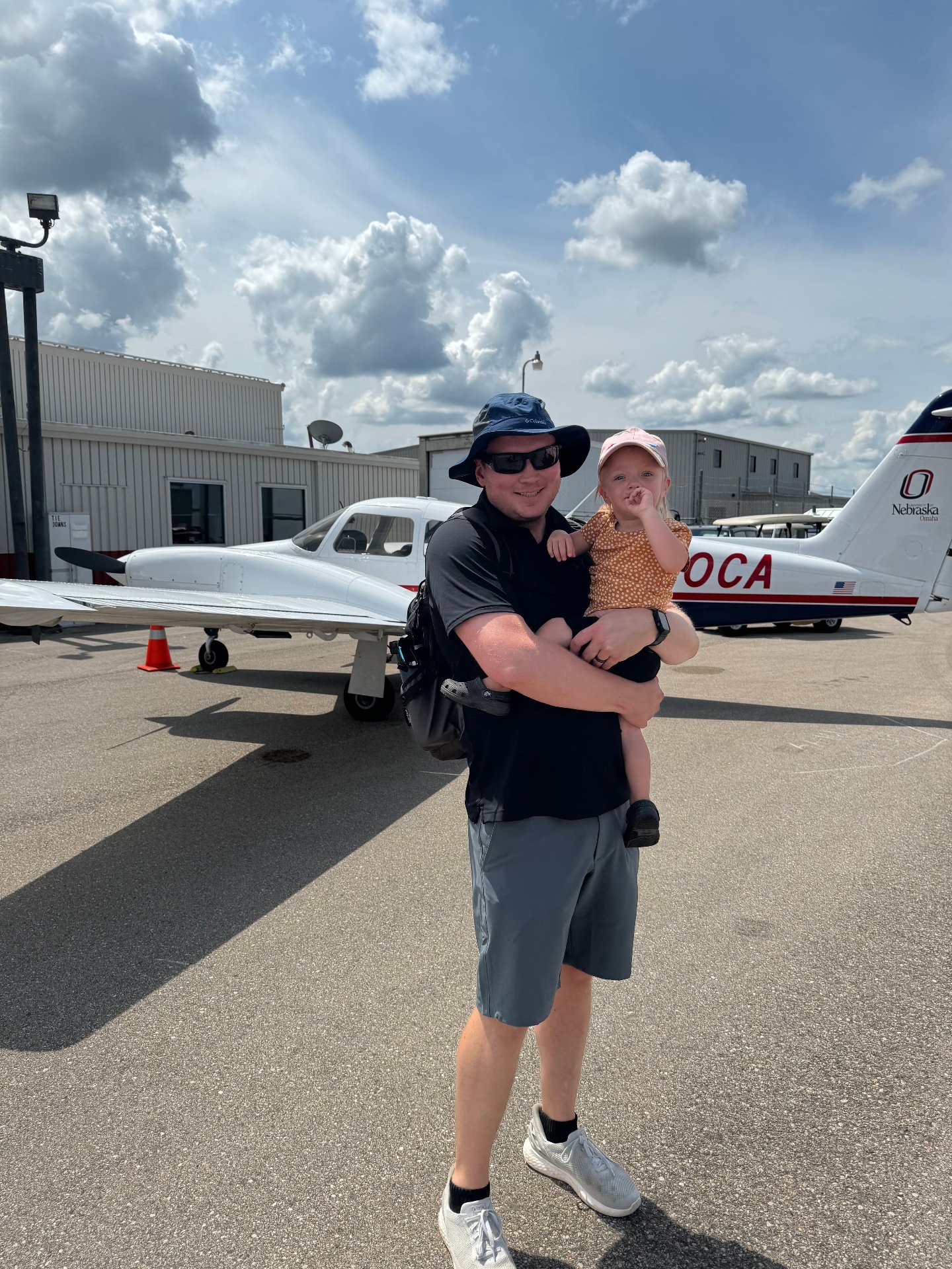 Man holding a child while standing in front of a small airplane