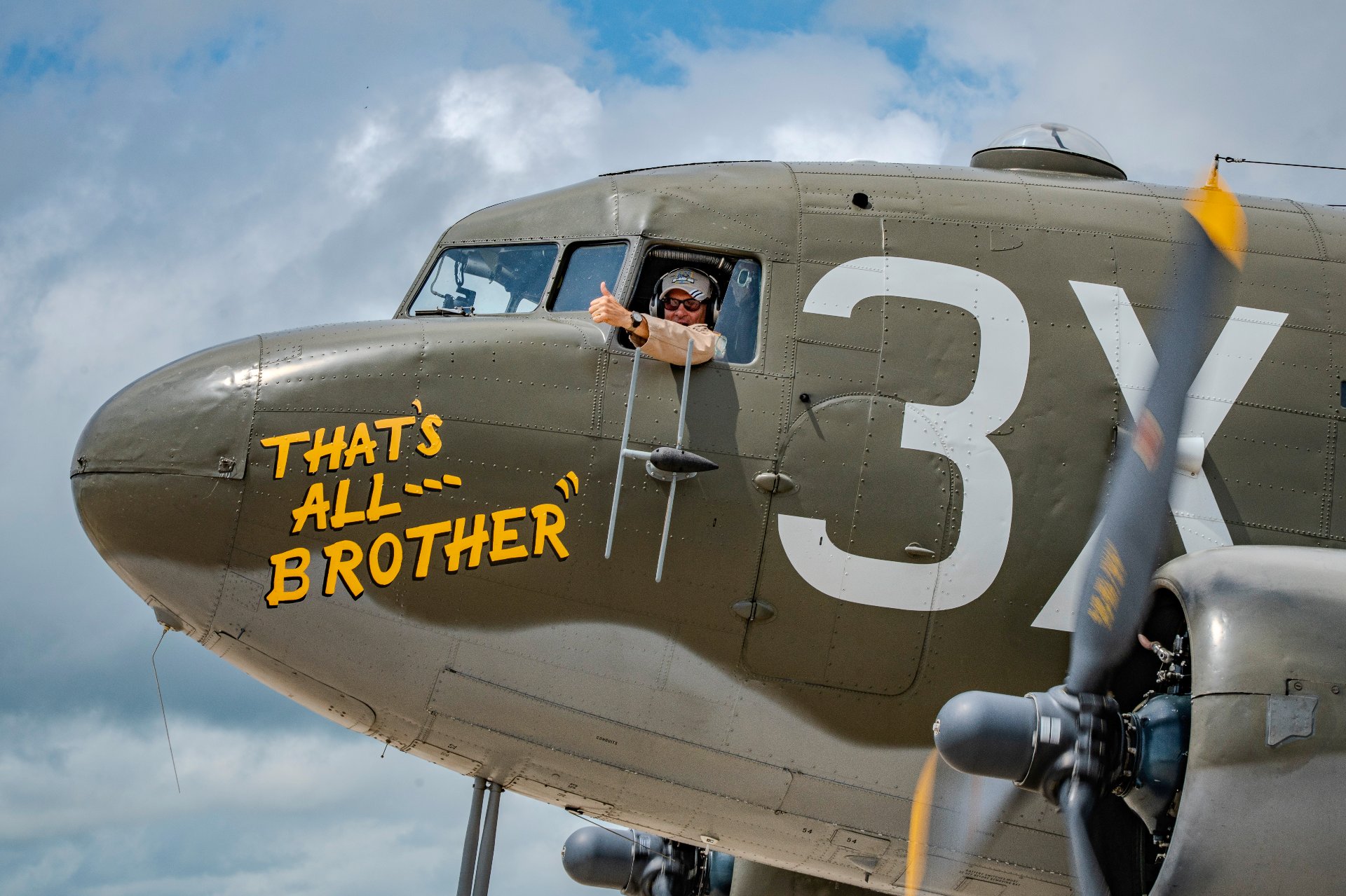 Pilot giving a thumbs-up from the cockpit of a vintage military aircraft.