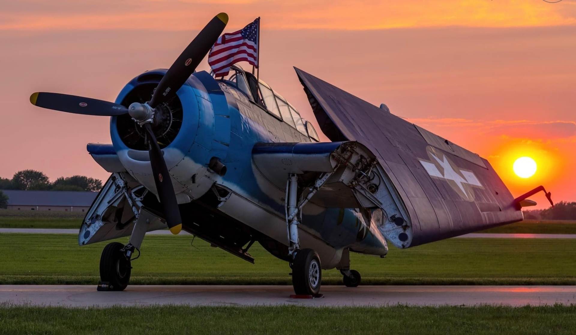 Vintage blue propeller aircraft parked at sunset with American flag on wing
