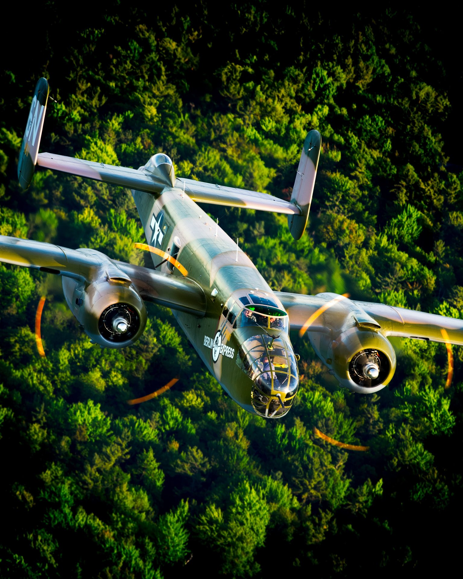 B-25 Berlin Express flying over a forest with propellers in motion