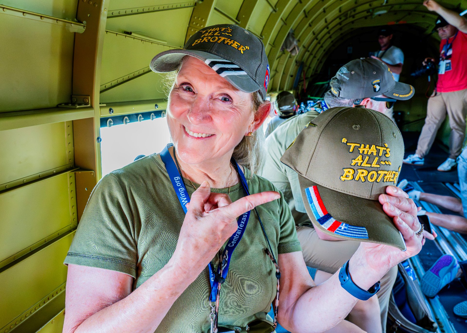 Passenger smiling inside That's All, Brother and pointing to a hat with the aircraft's name