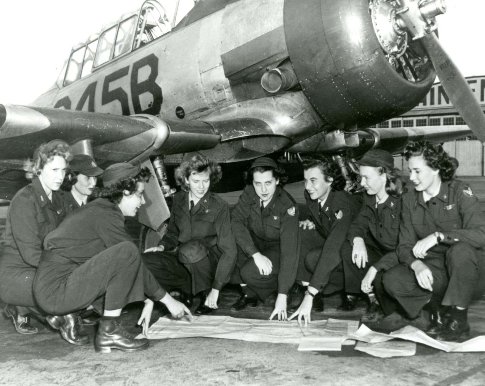 Group of Women Airforce Service Pilots kneeling beside a military aircraft and reviewing a map.