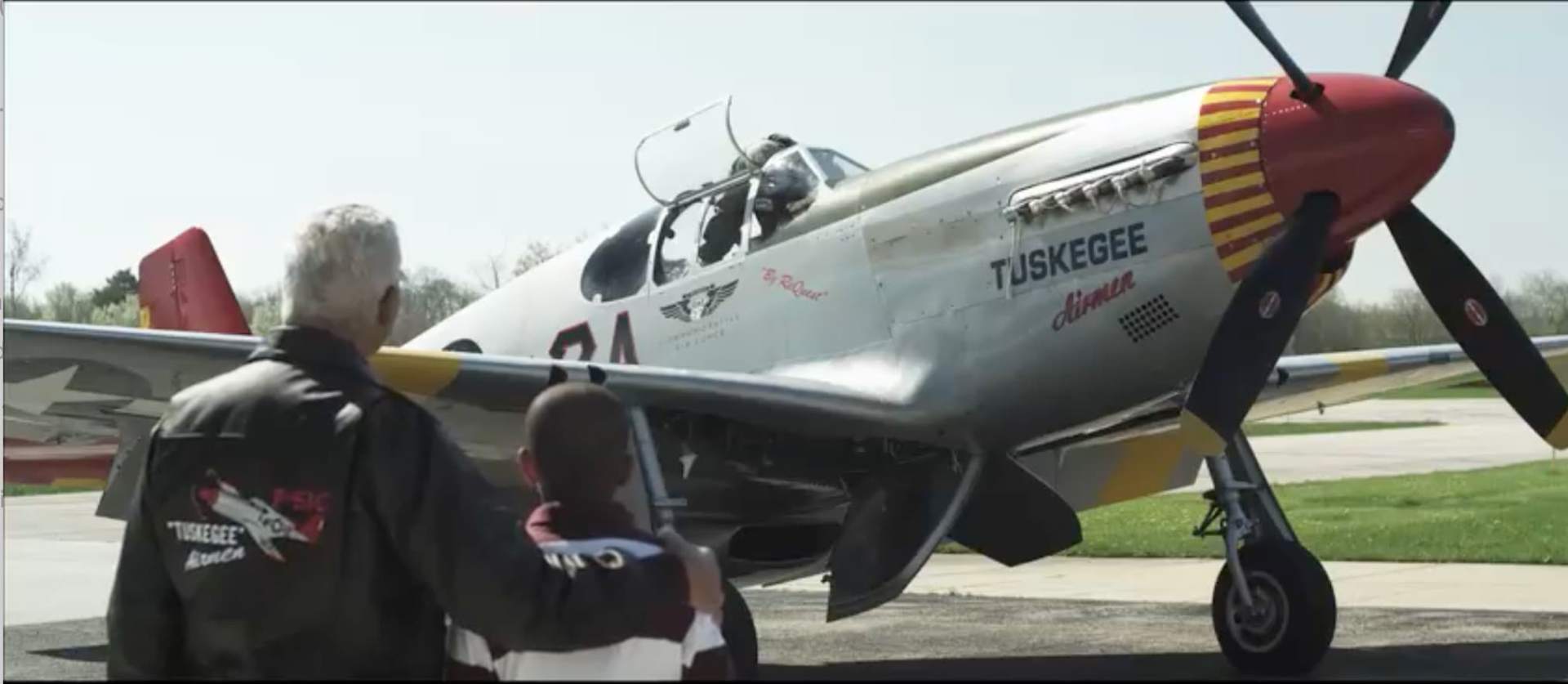 An older man and a young boy stand looking at a Tuskegee aircraft
