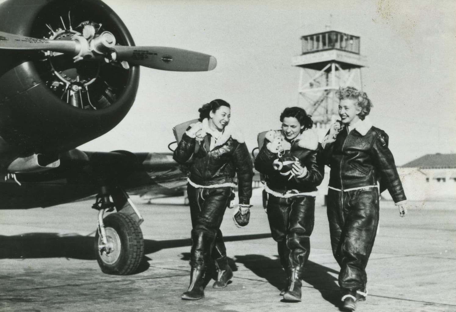 Three Women Airforce Service Pilots walking beside an aircraft and smiling together.