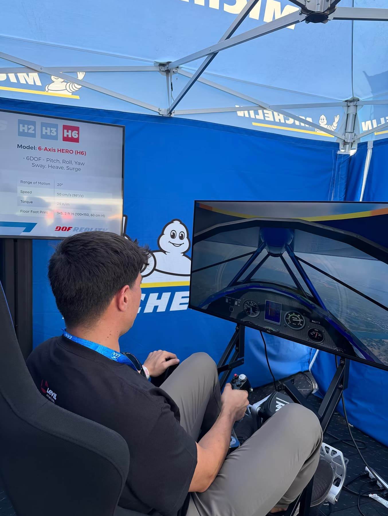 Person seated in a flight simulator chair controlling an aircraft simulation display at an aviation exhibit.