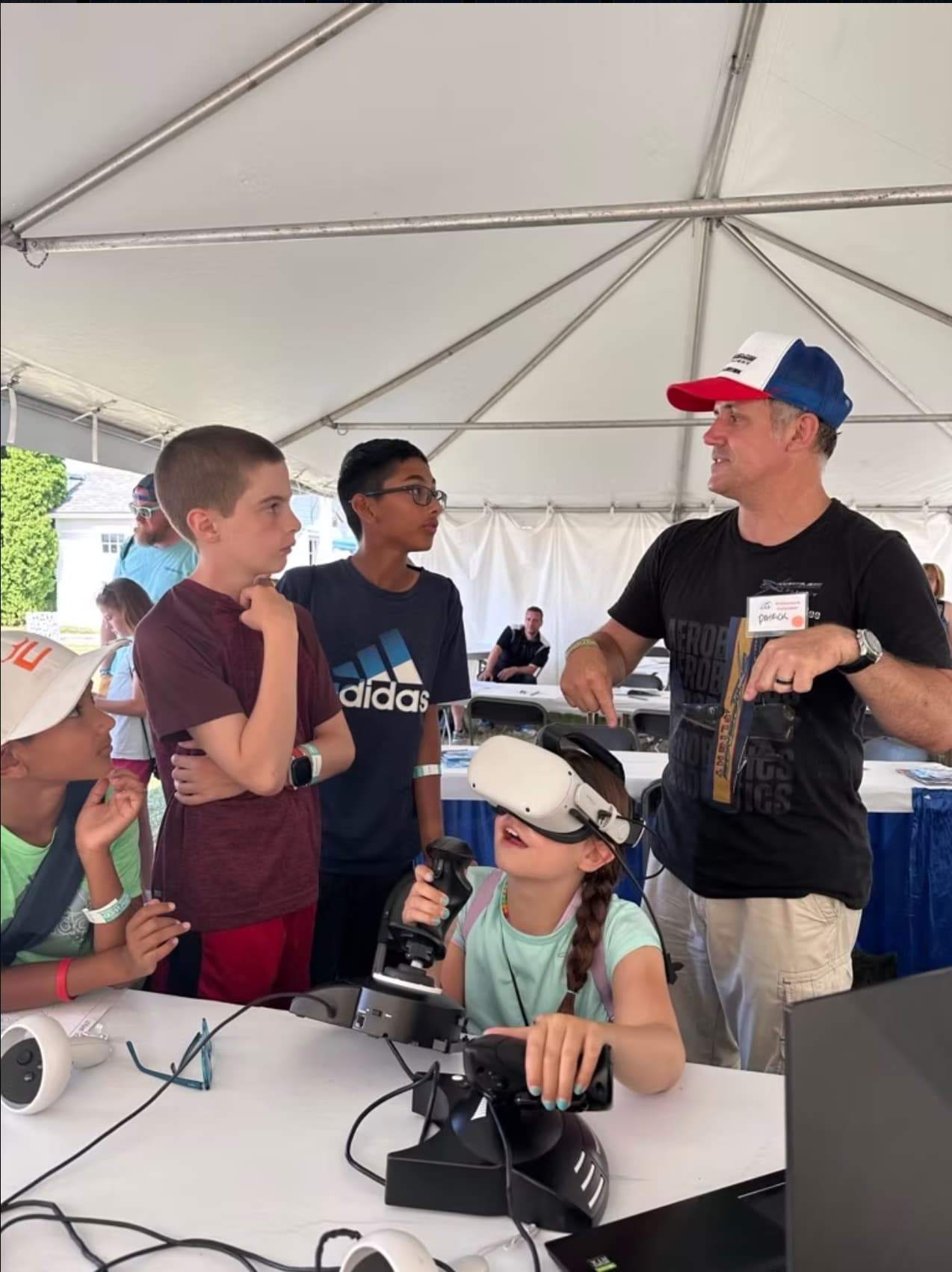Instructor guiding children as one participant uses a VR headset and flight controls at a STEM aviation activity.