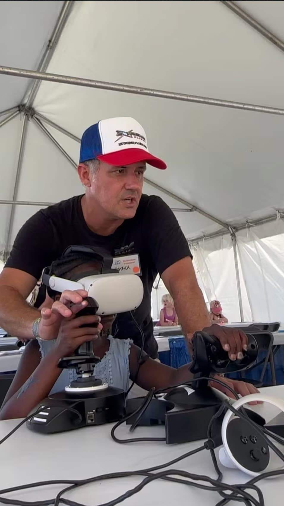 Instructor guiding children as one participant uses a VR headset and flight controls at a STEM aviation activity.