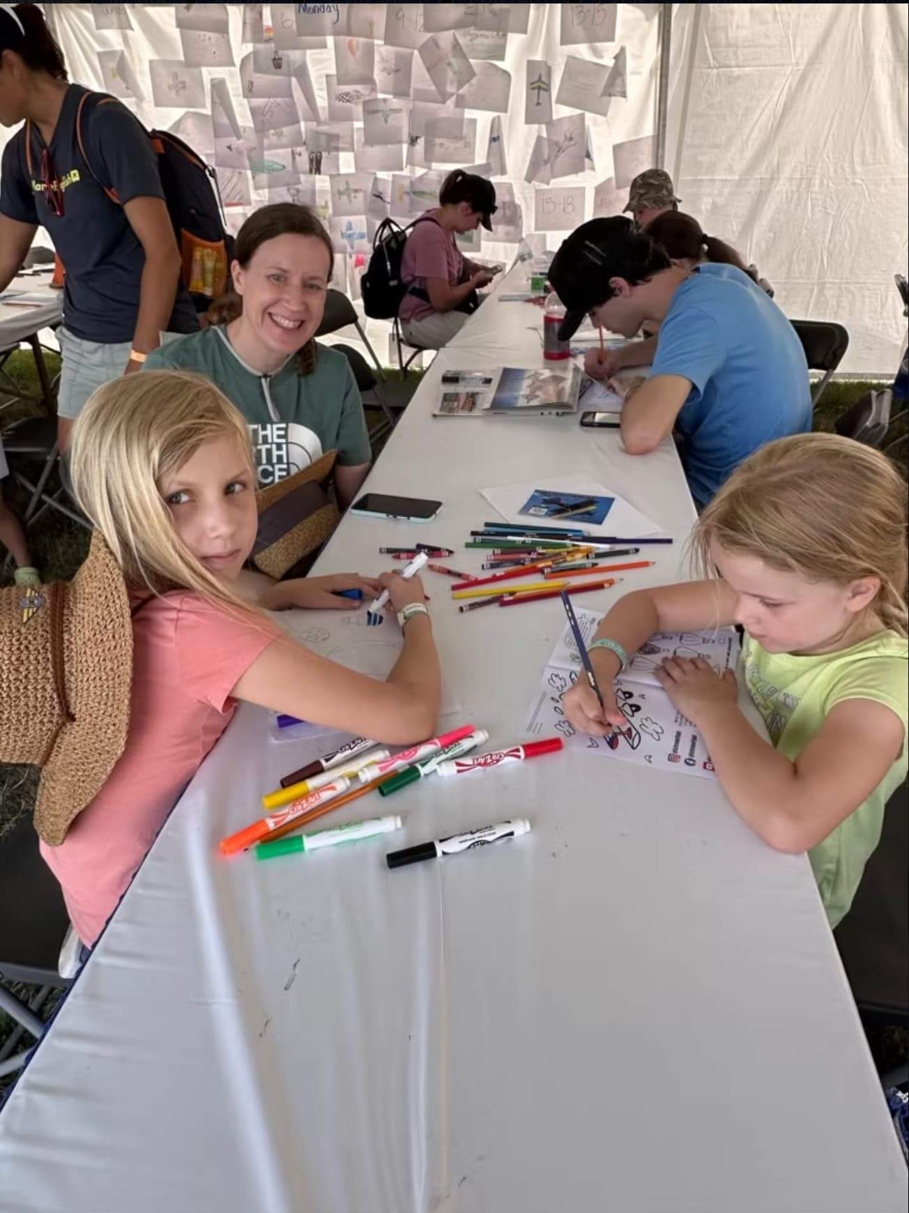 Children drawing airplanes with markers and pencils at an aviation-themed activity table.