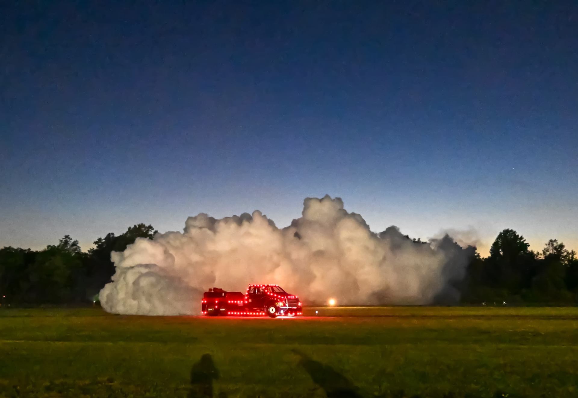 Truck lined with lights creating a cloud of smoke at dusk