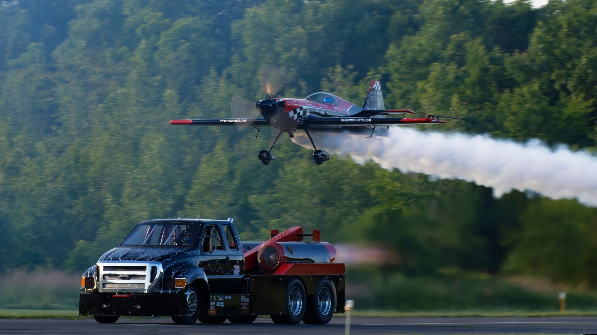 Jet truck racing down the runway with an airplane flying overhead
