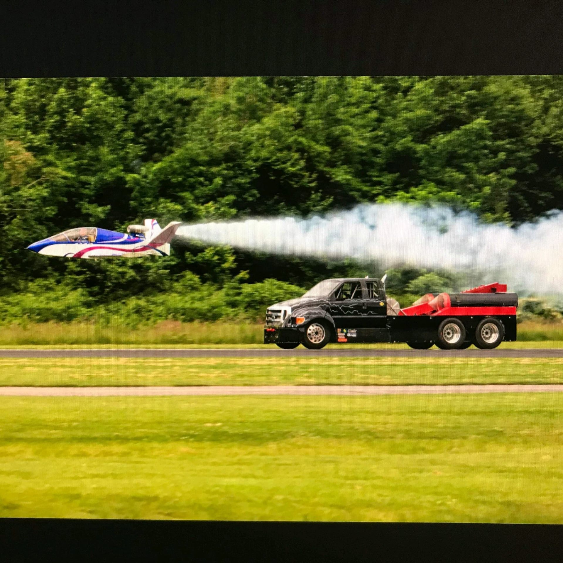 Jet car on the runway with a small airplane flying just in front of it
