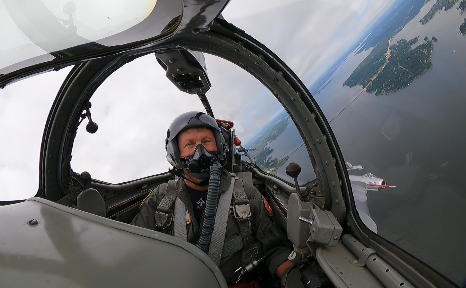 Randy Ball flying in the cockpit of a MiG-17F with two additional MiG-17s visible outside over a lake.
