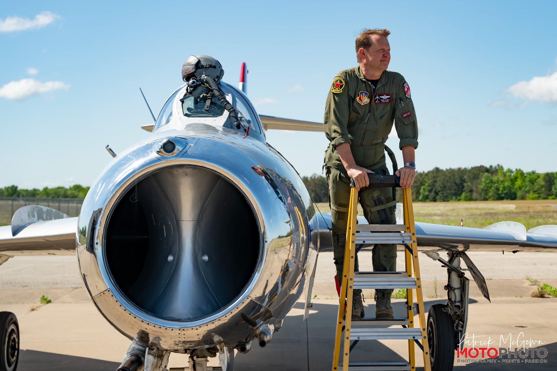 Randy Ball stands on a ladder beside his MiG-17F on the airfield, wearing a flight suit.