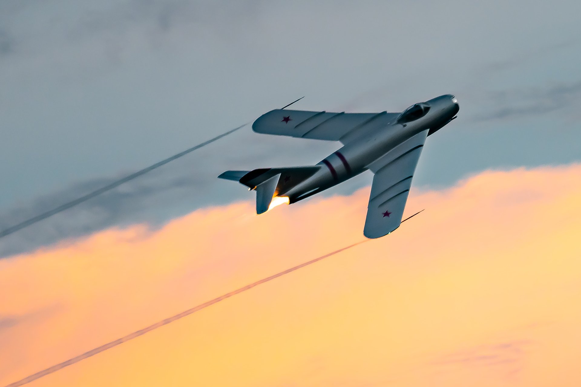 MiG-17F jet banking at sunset with afterburner flame visible.