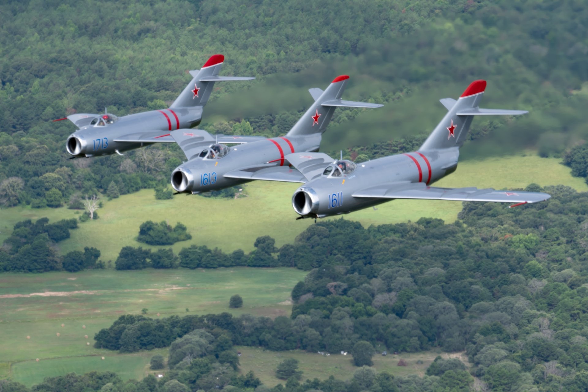 Three MiG-17F Jets flying over a forest.