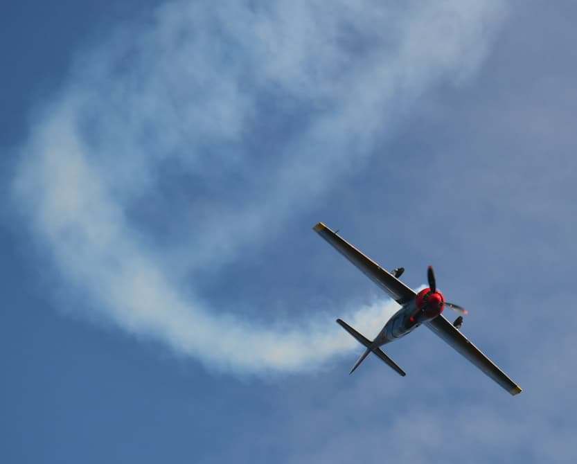 Yak-52 warbird performing an aerobatic turn with a smoke trail against a blue sky.
