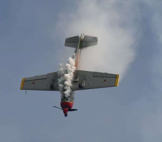 Yak-52 warbird flying inverted during an aerobatic maneuver with smoke trailing from the aircraft.