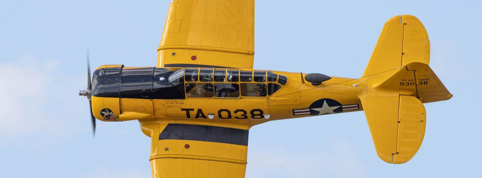 Top view of a yellow T-6 Texan aircraft in flight, showing its wings, cockpit, and U.S. Air Force markings.