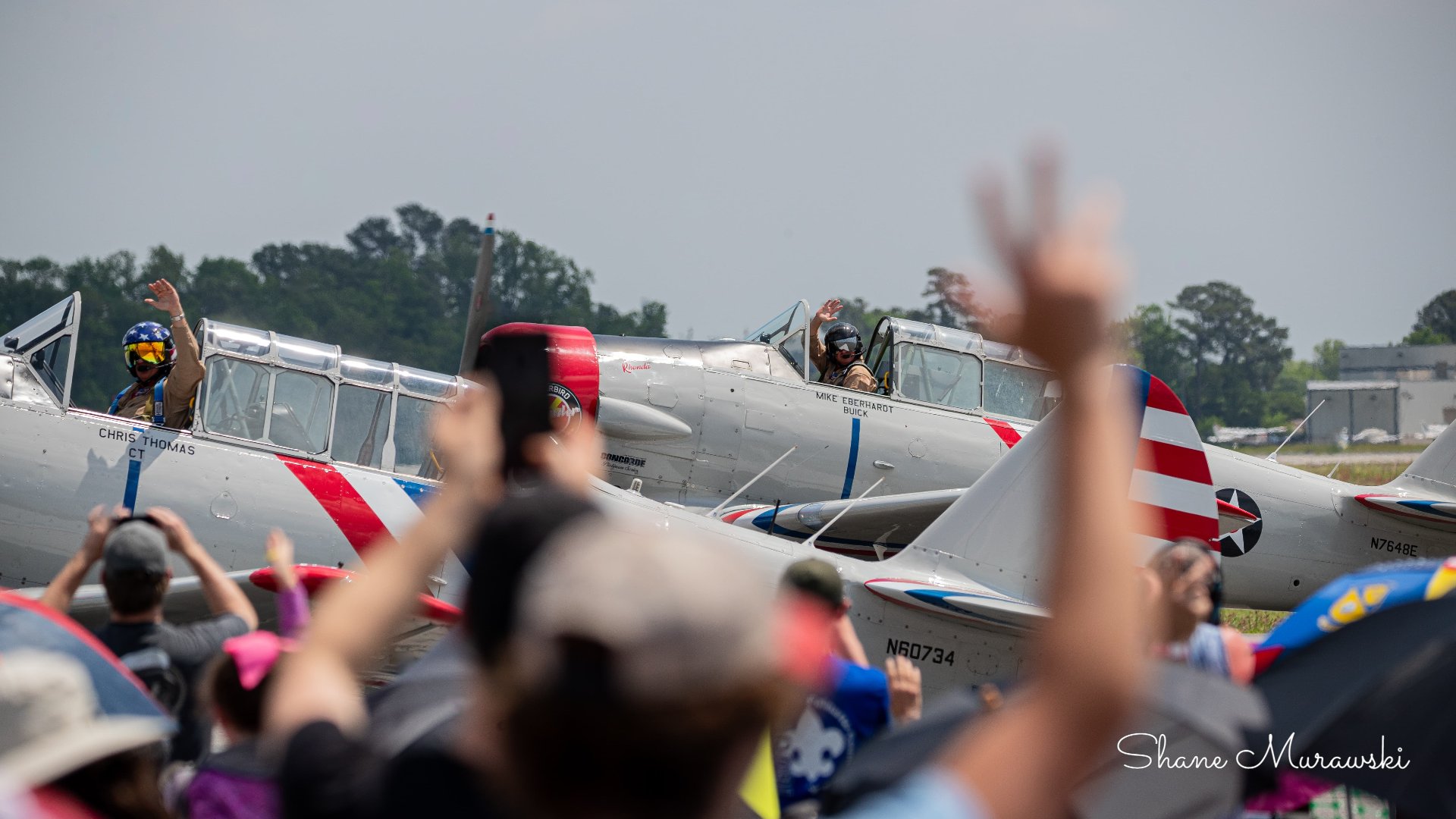Crowd greeting Warbird Thunder pilots in SNJ Texan aircraft on the ramp.