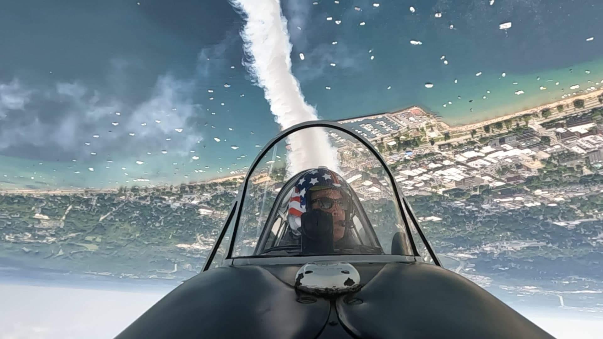 Inverted cockpit view from an SNJ Texan with smoke trail over the coastline.