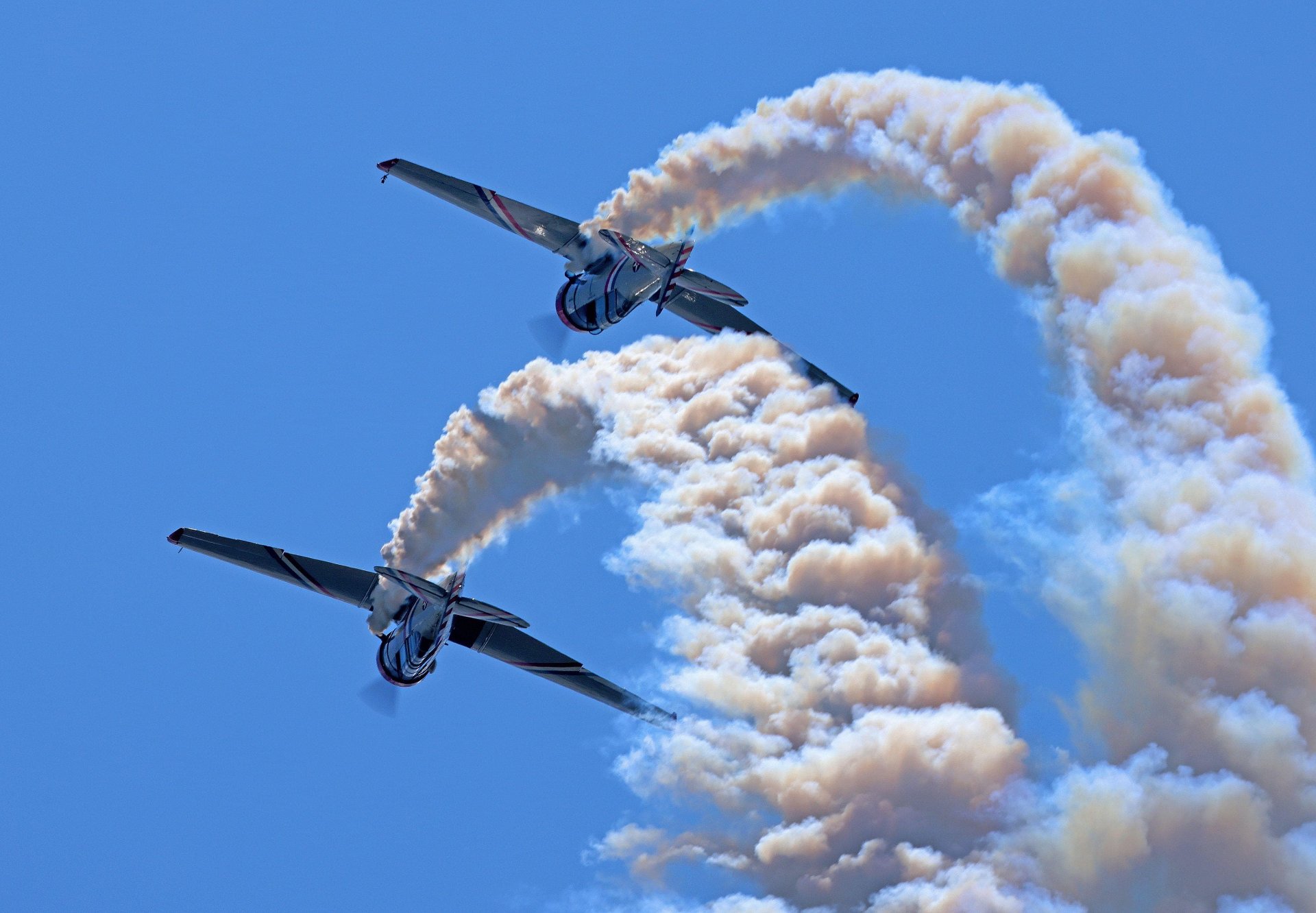 Two Warbird Thunder SNJ Texans carving mirrored loops through the sky, leaving thick curling smoke trails behind them.