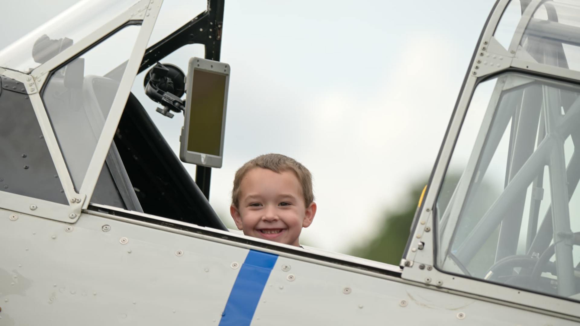 Kid sitting in the cockpit of a Warbird Thunder SNJ Texan during an airshow meet-and-greet, smiling at the camera.