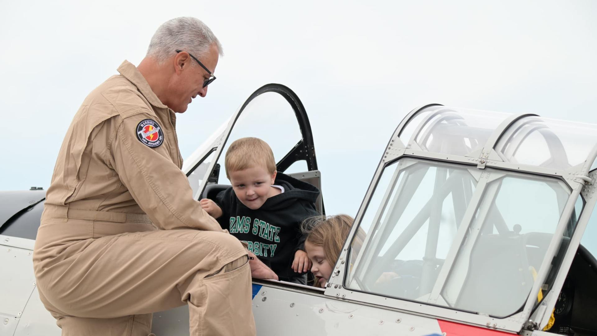 Warbird Thunder pilot helping two children sit in the cockpit of an SNJ Texan during an airshow meet-and-greet.
