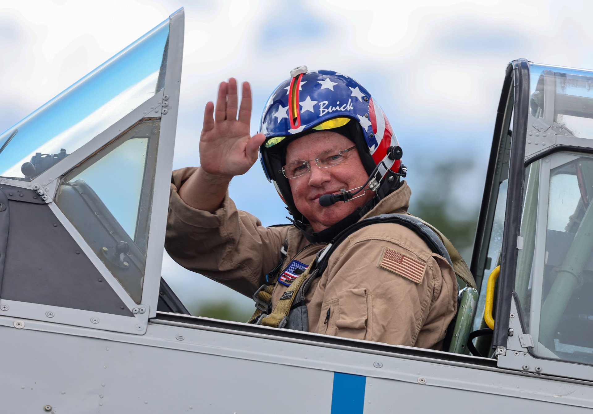 Mike “Buick” Eberhardt in a flight suit waving from the cockpit of an SNJ Texan during a performance.