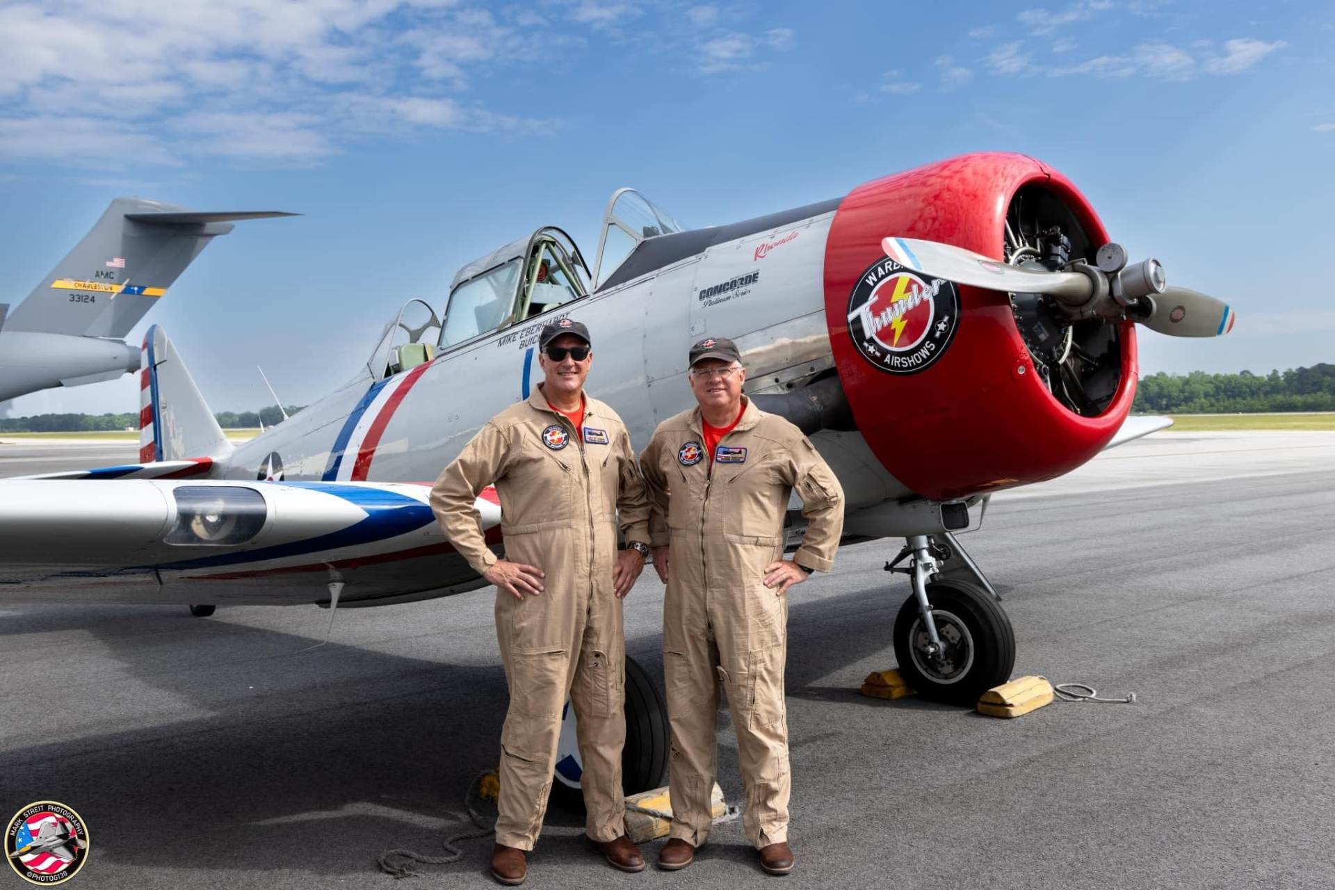 Pilot Chris “CT” Thomas and Mike “Buick” Eberhardt standing in front of their SNJ Texans, wearing flight suits smiling at the camera.