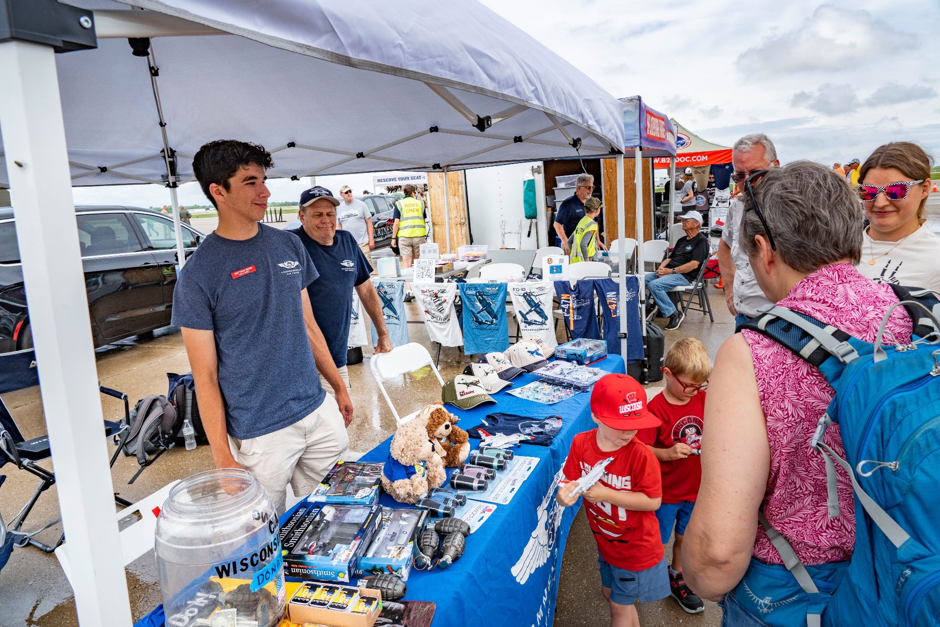 Families browse aviation merchandise and displays at a vendor booth during an outdoor airshow